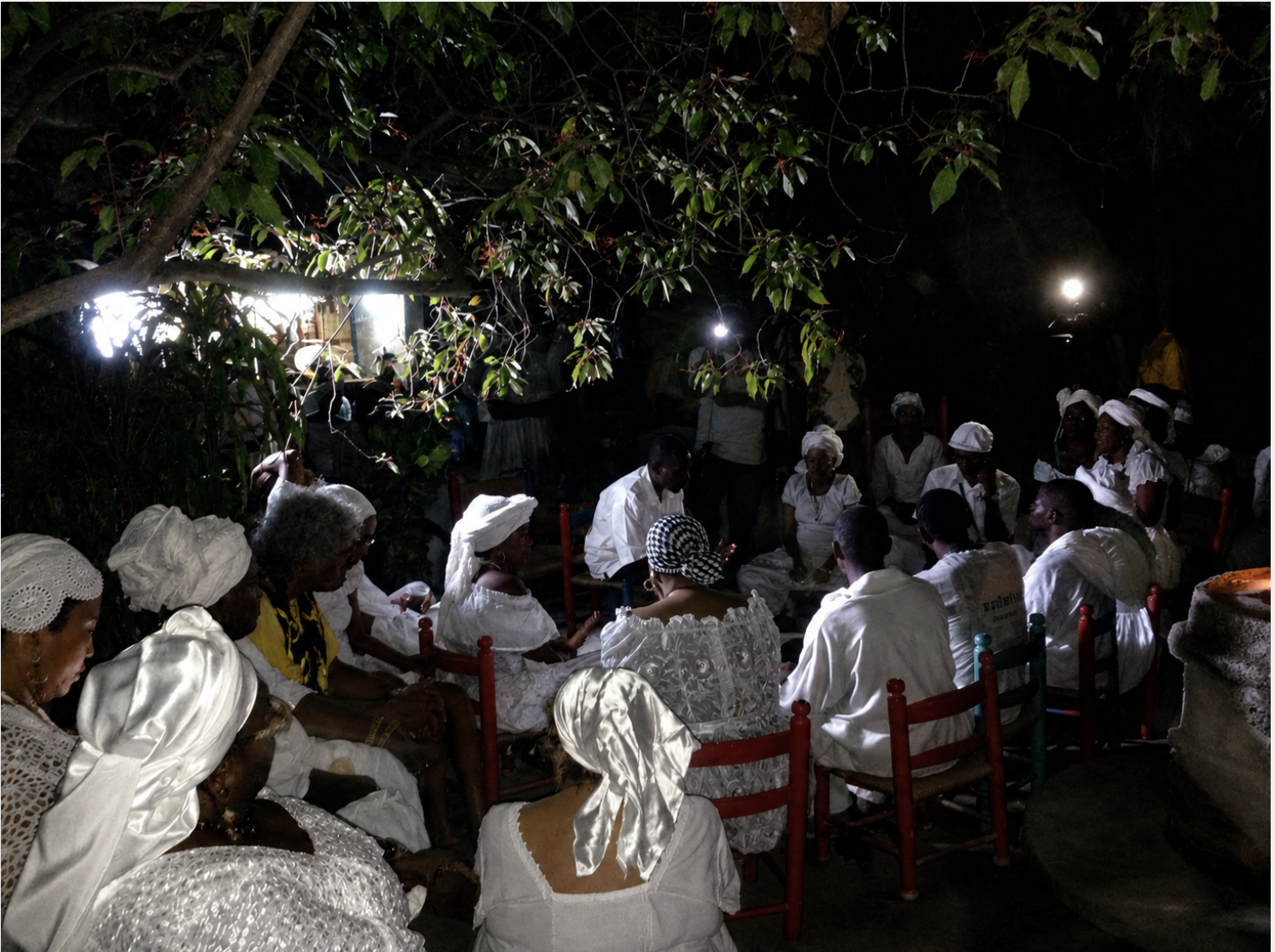 Nighttime Vodou ceremony with participants dressed in white seated in a circle